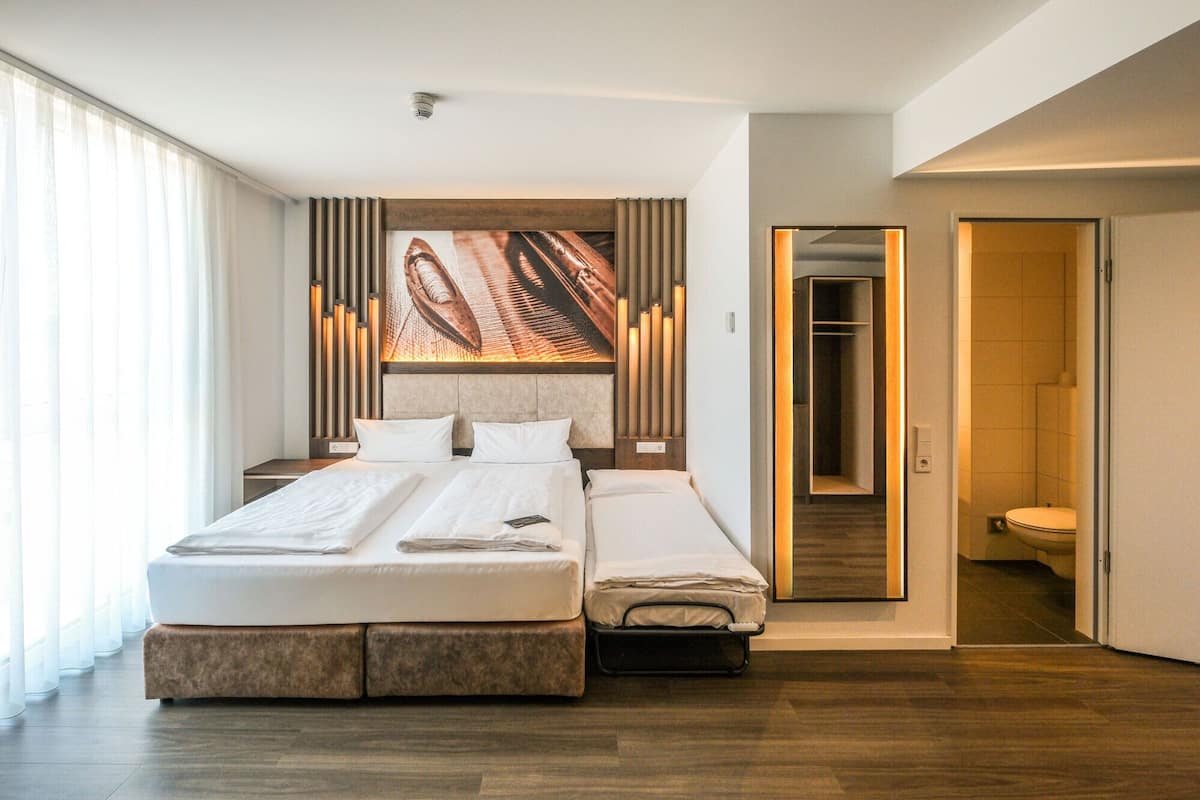Une chambre d’hôtel moderne avec un grand lit, une table de chevet, un miroir et vue sur la salle de bain.
