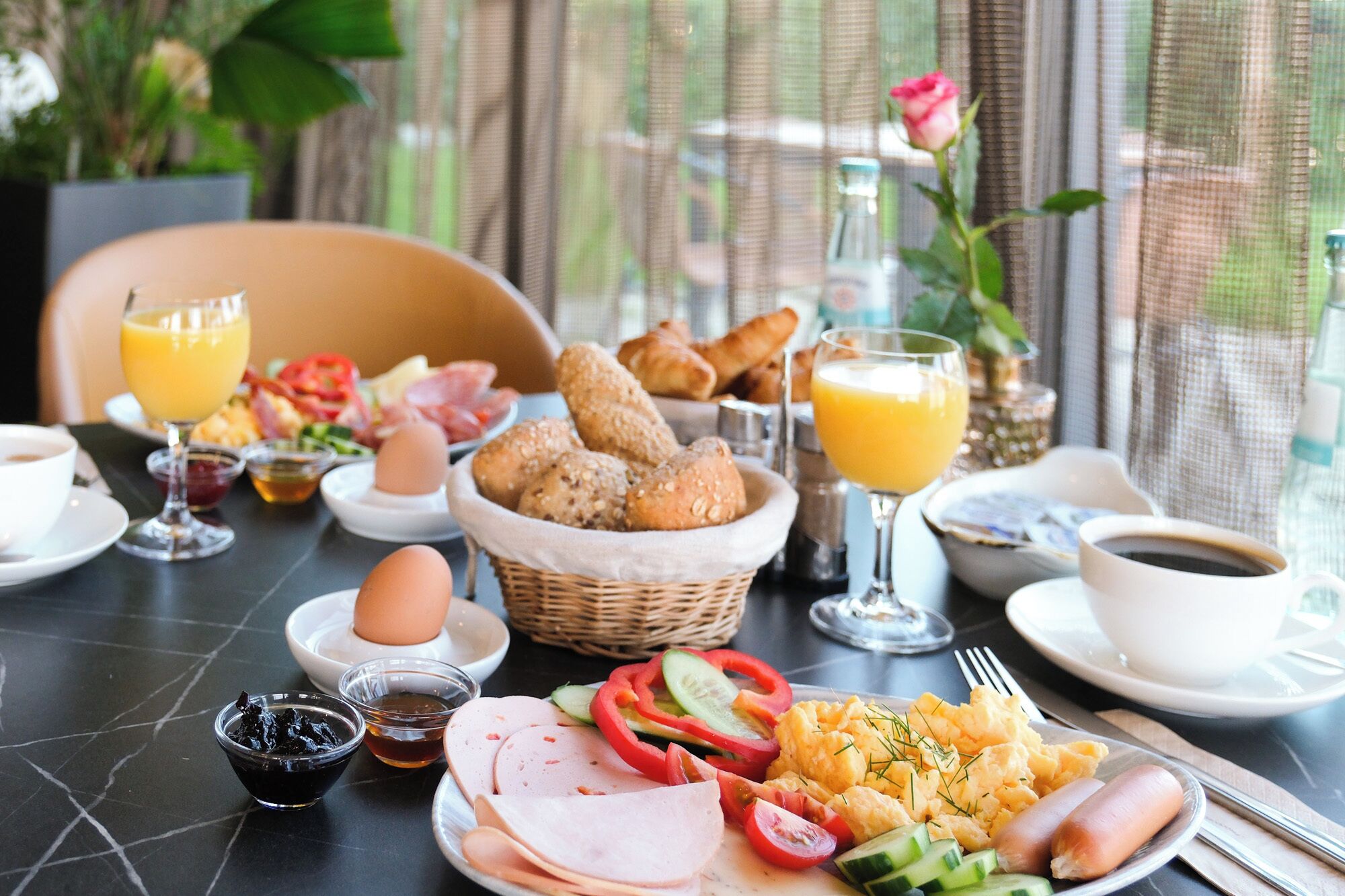 Ein Frühstückstisch mit verschiedenen Speisen, darunter Eier, Schinken, Würstchen und Gebäck, sowie Getränke und Beilagen.