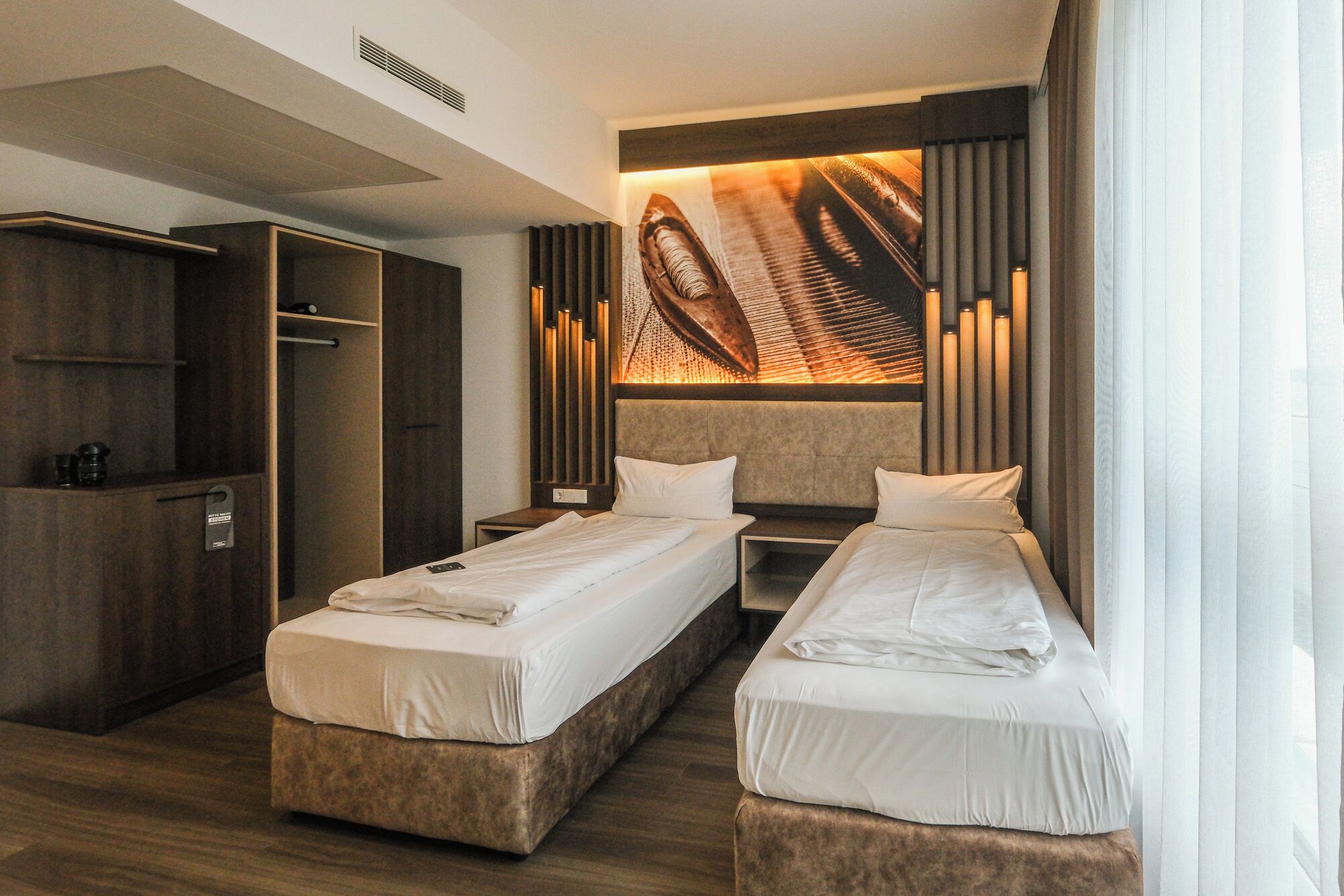 Habitación de hotel con dos camas, un armario e instalación artística única en la pared.