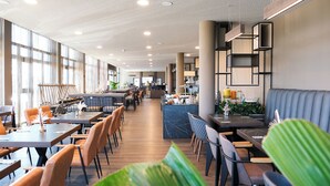 A modern hotel lobby with long tables, comfortable seating, and a reception area. - Tools Hotel Laichingen/Ulm (Laichingen)