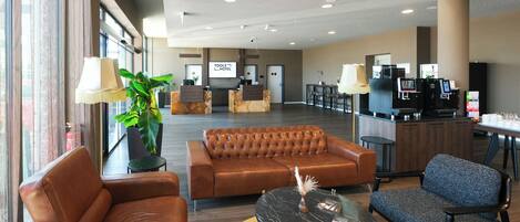 Un hall de hotel con sofás de cuero, una barra de café y un mostrador de recepción.