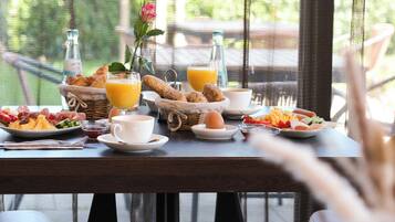 Een ontbijttafel met diverse etenswaren, waaronder brood, eieren en fruit, op een balkon met uitzicht op groen.