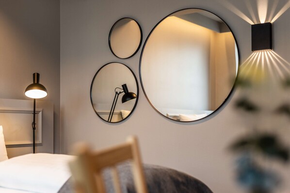 Une chambre d’hôtel moderne équipée d’un lit, d’une lampe de bureau et de trois miroirs fixés au mur.