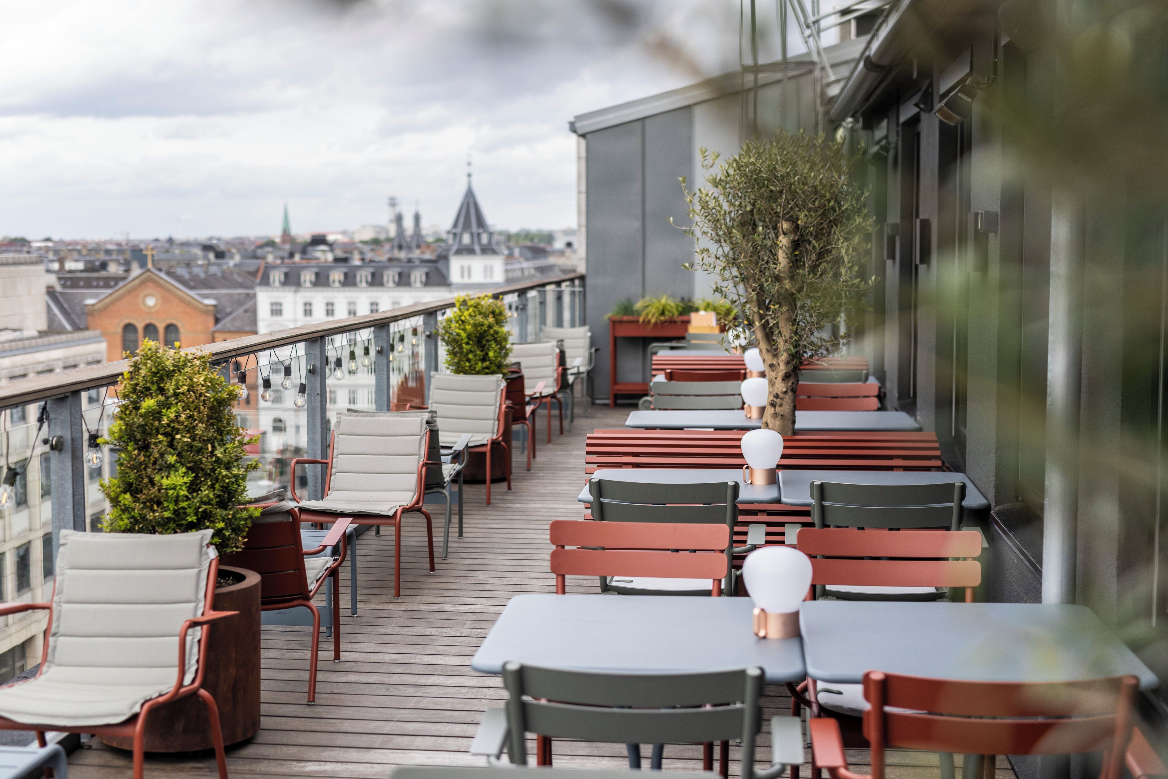 Una terraza en la azotea con mobiliario exterior, vistas de la ciudad y la cúpula de una iglesia a lo lejos.