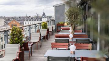 Una terraza en la azotea con mobiliario exterior, vistas de la ciudad y la cúpula de una iglesia a lo lejos.