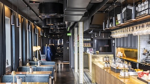 Un interior de restaurante moderno con mesas de madera y asientos tapizados en azul, una zona de bar con cristalería y un revoque de azulejos.