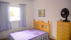 Ein Schlafzimmer mit einem hölzernen Bett, einem Schminktisch, einem Ventilator und einem Fenster mit Vorhängen.