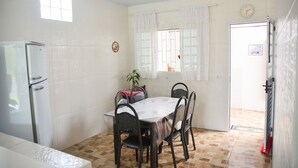 Ein Essbereich mit Tisch, Stühlen, einem Kühlschrank, einer Uhr und einem fenster mit Vorhängen.