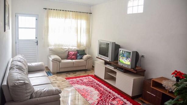 Ein Wohnzimmer mit einer Couch, einem Fernseher, einem Fenster mit Vorhängen und einem roten Teppich.
