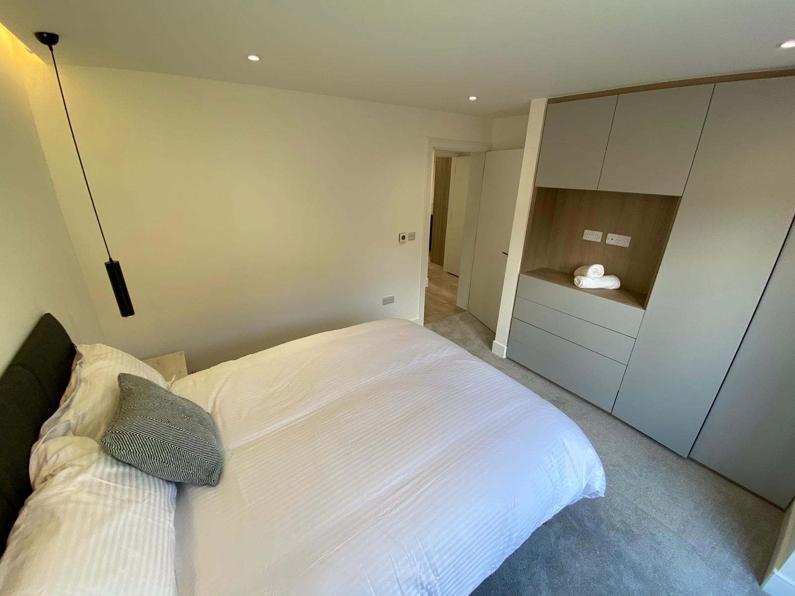 A modern bedroom with a large bed, a wardrobe, and a hanging light fixture.
