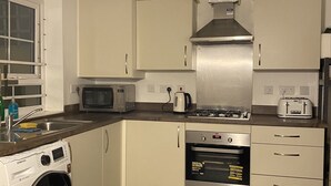 A compact kitchen with a washing machine, microwave, toaster, and oven. - Serenity by the Canal House near City Centre with 2 Parking ( Sleeps 5 ) (Coventry)