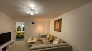 A living room with a sofa, a TV stand, a floor lamp, and a painting on the wall. - Serenity by the Canal House near City Centre with 2 Parking ( Sleeps 5 ) (Coventry)