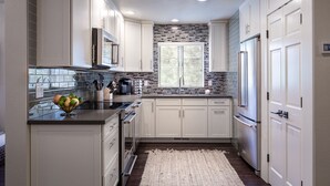 A modern kitchen with white cabinets, a stainless steel refrigerator, and a window with a view of trees. - 101McCloud 2BR/2BA Incline Village | Hot Tub (Incline Village)