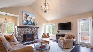 A spacious living room with a stone fireplace, comfortable seating, a flat-screen TV, and a large window offering a view of the outdoors. - 101McCloud 2BR/2BA Incline Village | Hot Tub (Incline Village)