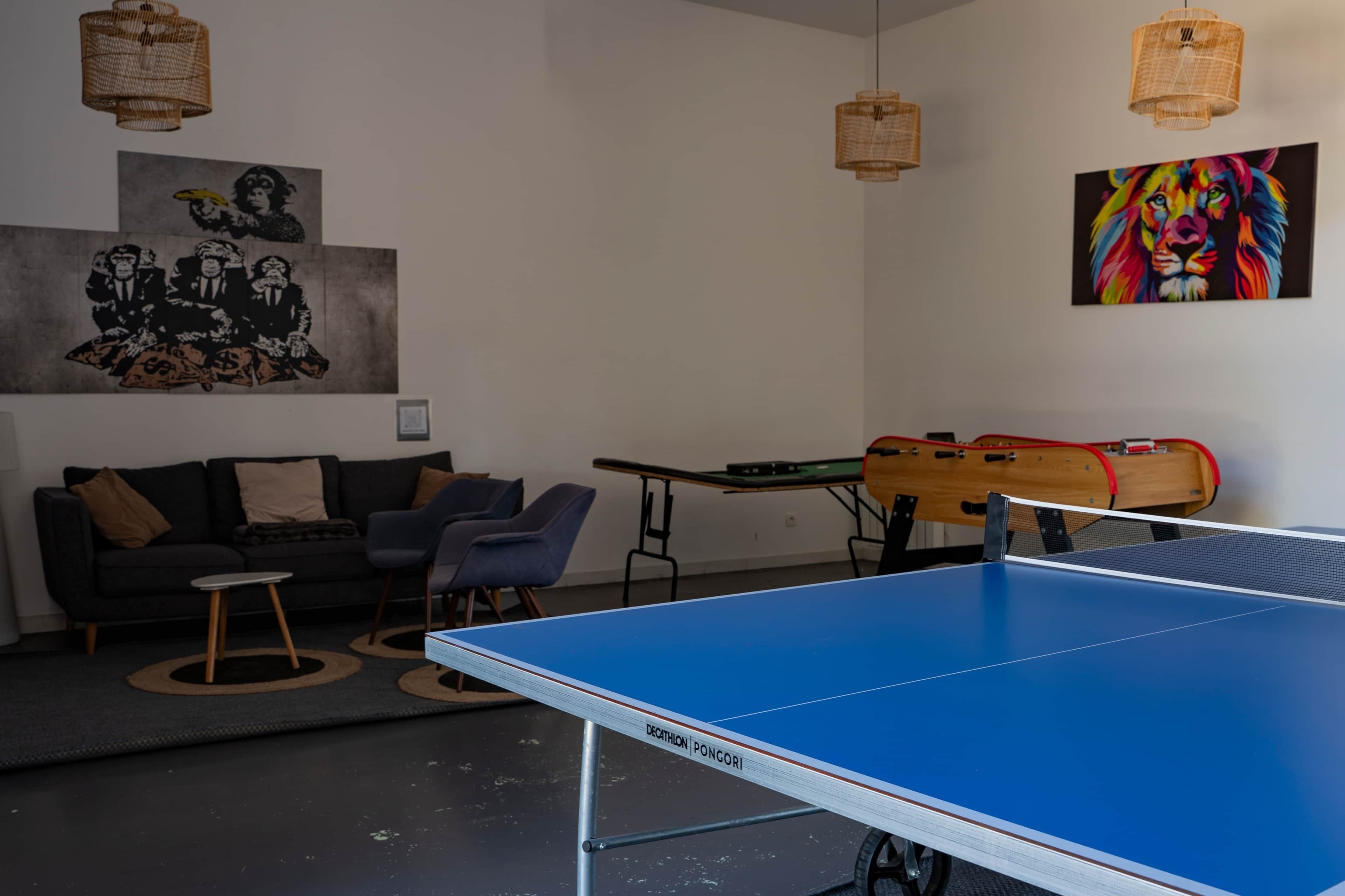 Une pièce avec une table de ping-pong, un canapé et deux chaises. Il y a deux tableaux accrochés au mur.