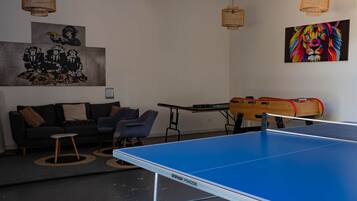 Une pièce avec une table de ping-pong, un canapé et deux chaises. Il y a deux tableaux accrochés au mur.