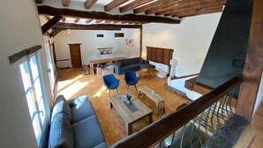 Amplia sala de estar con techo alto, vigas de madera, un sofá grande, dos sillones, una mesa de centro y una mesa de comedor.