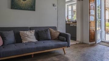 A grey sofa with multiple cushions, a kitchen area with a dishwasher, and a wooden door leading outside.