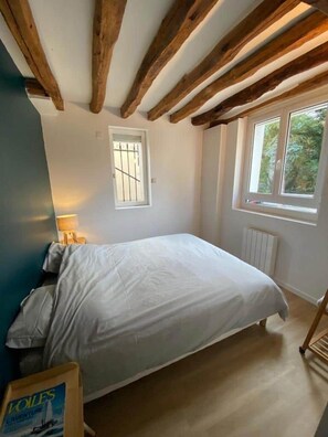 Un dormitorio con cama, ventana, radiador y techo de madera.