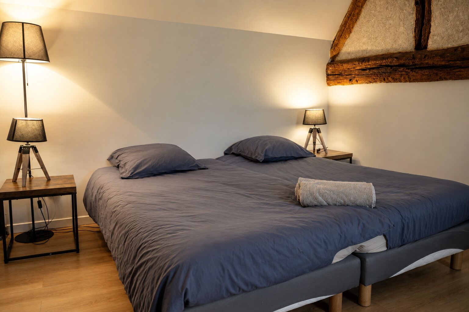 A bedroom with a large bed, two bedside tables with lamps, and a wooden ceiling beam.