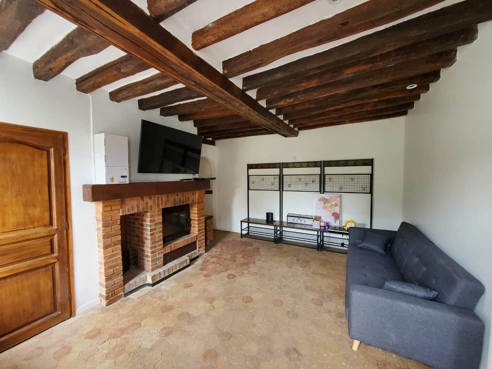 Ein Wohnzimmer mit freiliegenden Holzbalken, einem Kamin aus Backstein, einem Flachbildfernseher und einem Sofa.