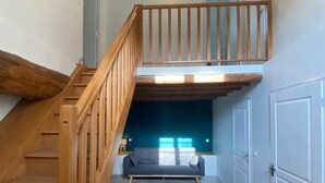 Una escalera conduce a un dormitorio tipo altillo con una cama, un sofá y una ventana.