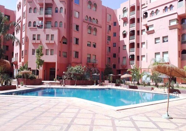 Un bâtiment rose doté d’une piscine et d’un espace extérieur aménagé pour s’asseoir.
