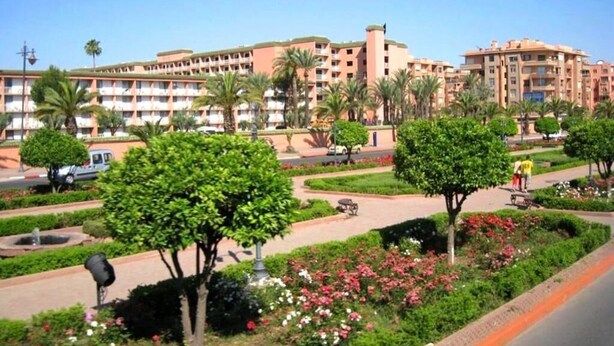 Ein Hotel mit mehreren Etagen, Palmen und einem gepflegten Garten mit Blumen und Sträuchern.