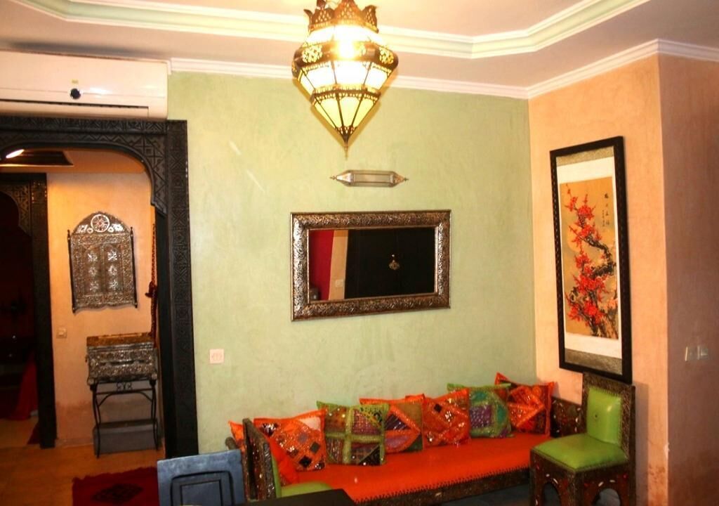 Una habitación con un sofá verde, un espejo y una lámpara tradicional.