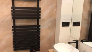 Um banheiro moderno com parede de mármore bege, porta-toalhas preto, pia branca e espelho.