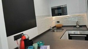 Cozinha moderna com armários brancos, painel de fundo preto, pia de aço inoxidável e forno embutido.