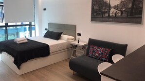 Quarto de hotel moderno com uma cama, um sofá, uma escrivaninha e uma janela ampla.