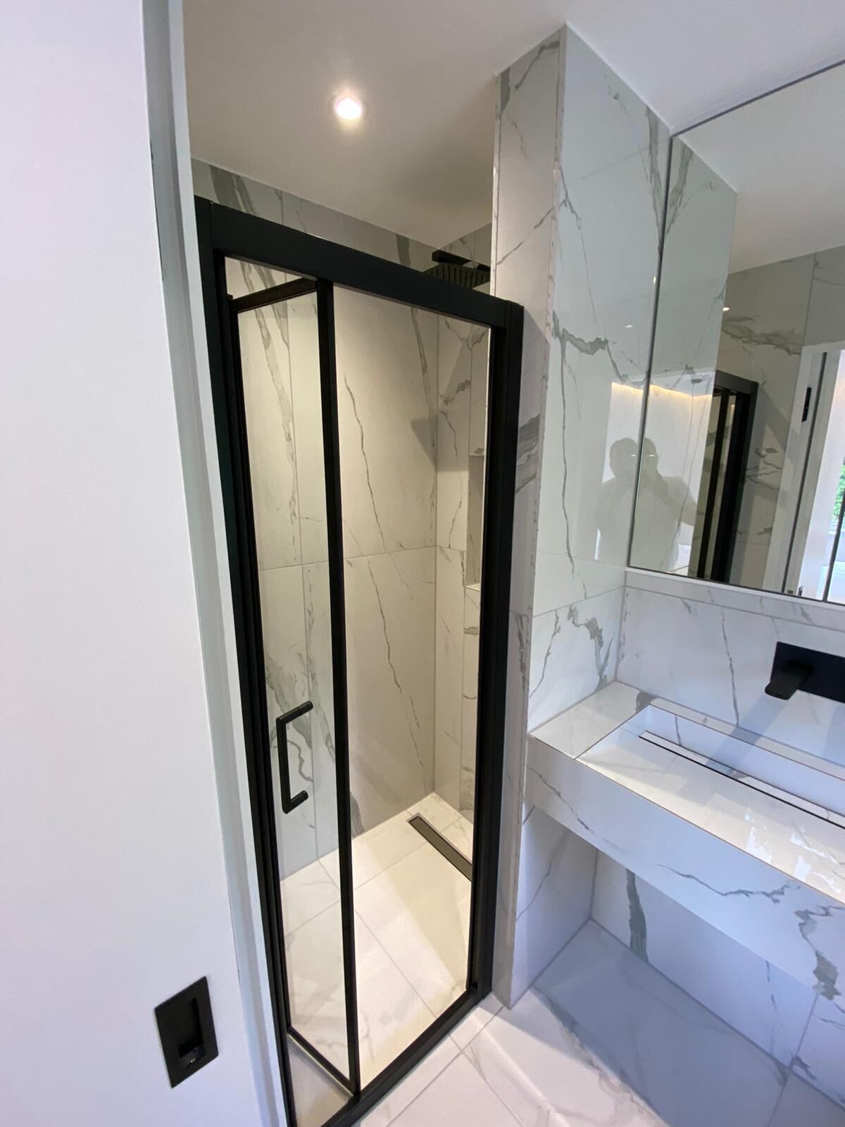 Ein modernes Badezimmer mit einer Glaskabine zur Dusche, Marmorwänden und einem großen Spiegel.