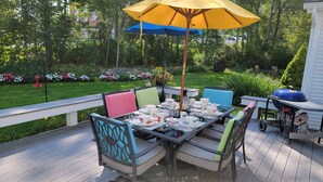 An outdoor patio with a table set for a meal, surrounded by chairs with colorful cushions.