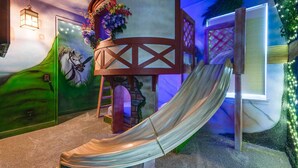 Un espace de jeux avec un toboggan, une structure d’escalade en bois et une fresque murale.