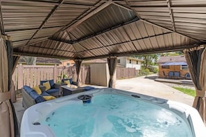 A hot tub under a covered patio with a sofa and cushions.