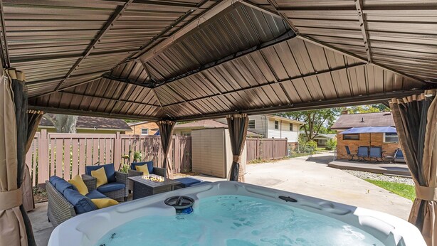 A covered outdoor hot tub area with a patio, seating, and a view of the neighborhood. - Hot Tub | Sauna | Fire Pit | Outdoor Living | Elegant Ranch (Ann Arbor)