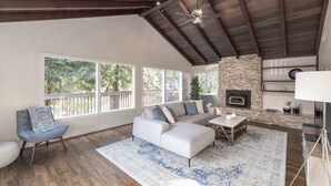 Un salón amplio con un sofá blanco modular, piso de madera y chimenea de piedra.