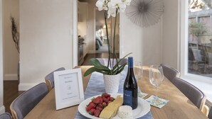 Una mesa de comedor con un cartel de bienvenida enmarcado, un plato de fresas y queso, una botella de vino y una copa.