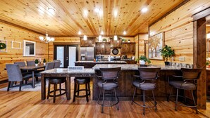A wooden cabin interior with a kitchen, dining area, and bar.