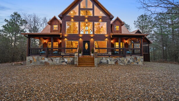 A large log cabin with a stone foundation, multiple windows, and a prominent front porch.