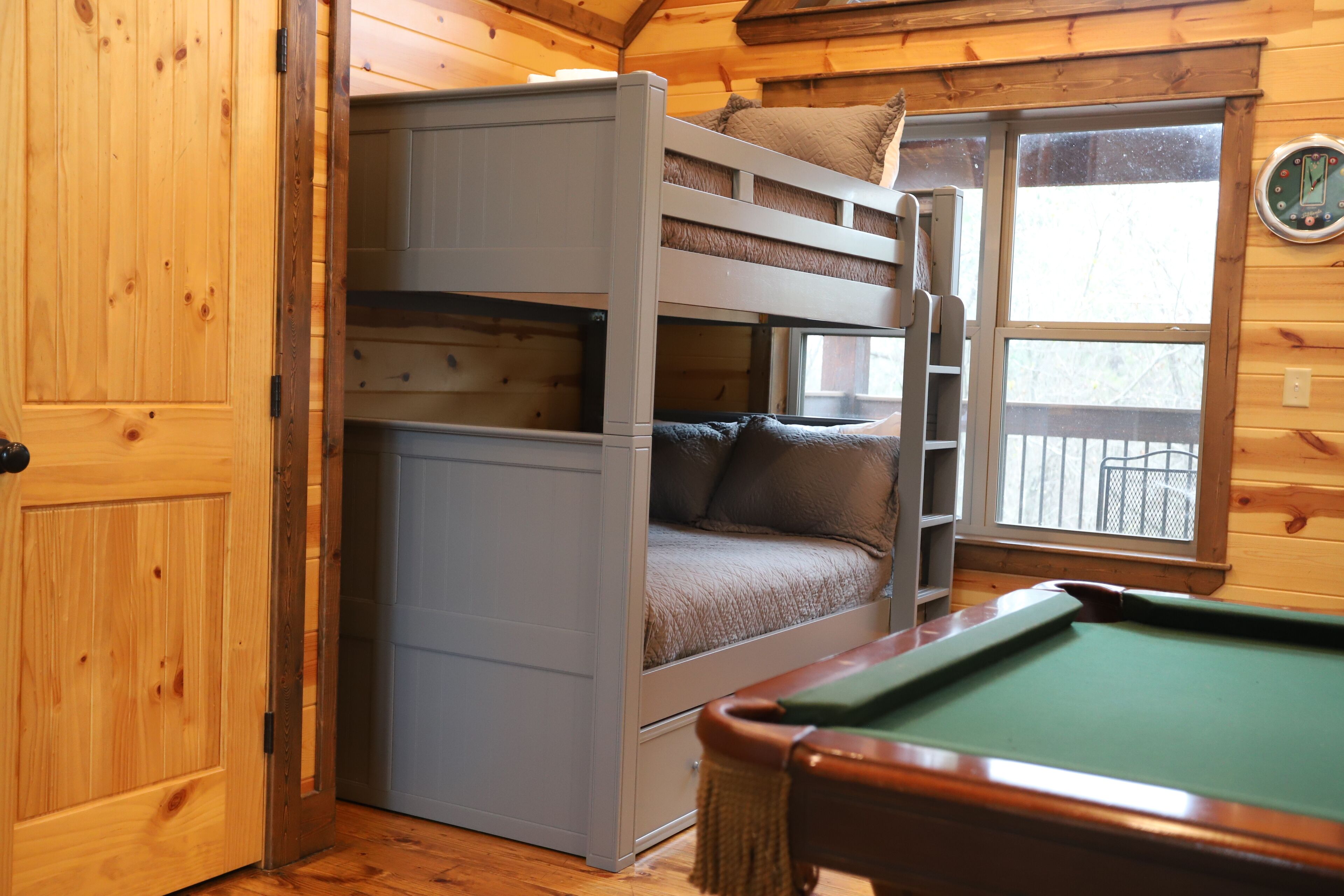 A bunk bed with a ladder, a pool table, and a window with a view of a snowy landscape.