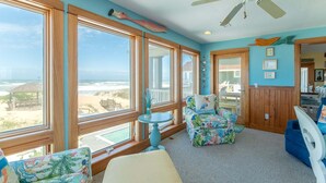 A room with large windows, a ceiling fan, and a view of the beach. - Beach Royalty - Nags Head MP 15.5, Luxury Oceanfront, Private Walk to Beach, Elevator, Pool, Hot Tub (Nags Head)