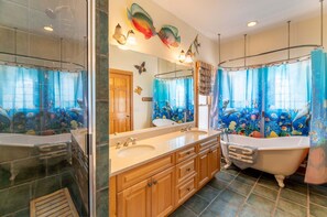 Ein Badezimmer mit einer Badewanne, zwei Waschbecken, Holzschränken, einem großen Spiegel und einem Duschvorhang mit Fischmotiv.