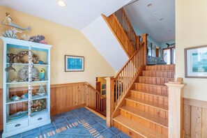 Eine Holztreppe mit einem blau gemusterten Teppich, eine weiße Wand mit einem gerahmten Bild und ein blaues Regal mit Dekorationen.