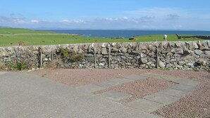 Un muro de piedra con vista al mar y campos verdes.