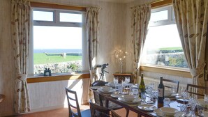 Comedor con mesa lista para cuatro personas, vista al mar y decoración rústica.