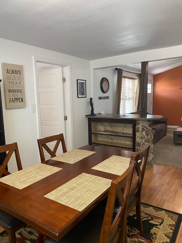 Un coin repas avec une table et des chaises en bois, un mur décoratif en pierre, une horloge et un panneau d’accueil.
