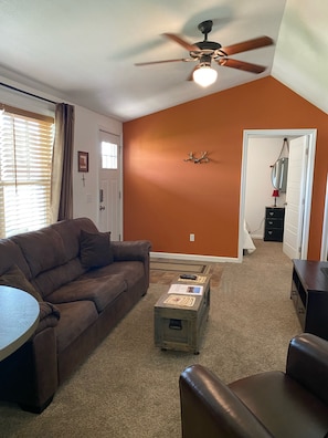 Un salon avec un canapé en cuir marron, une table basse sur laquelle se trouvent des papiers, un ventilateur de plafond et un mur orange.