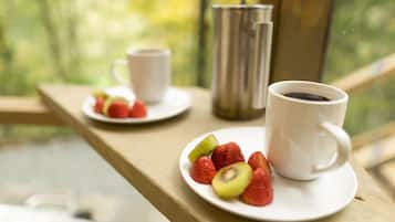 Une table en bois près d’une fenêtre est dressée pour le petit-déjeuner : on y trouve une tasse de café et une assiette de fraises et de kiwis.
